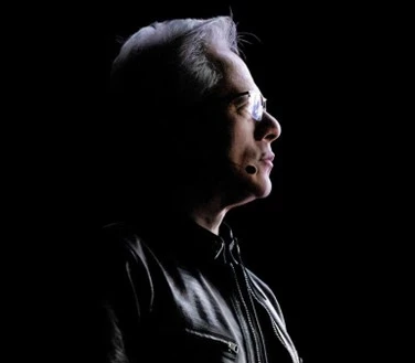 Jensen Huang in profile on a dark stage, wearing a headset microphone.