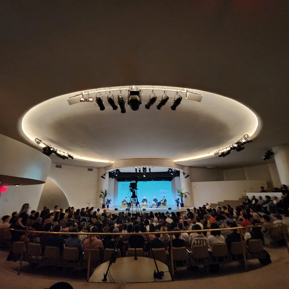 A full auditorium beneath a circular ceiling light.