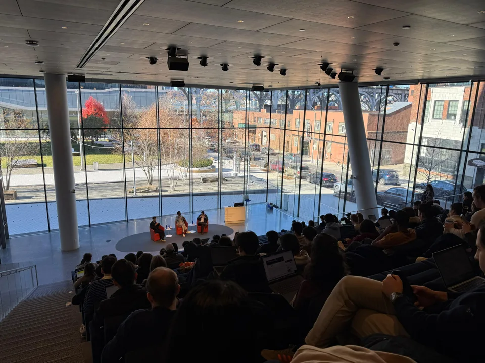 An audience listening to a conversation in a sunlit auditorium.